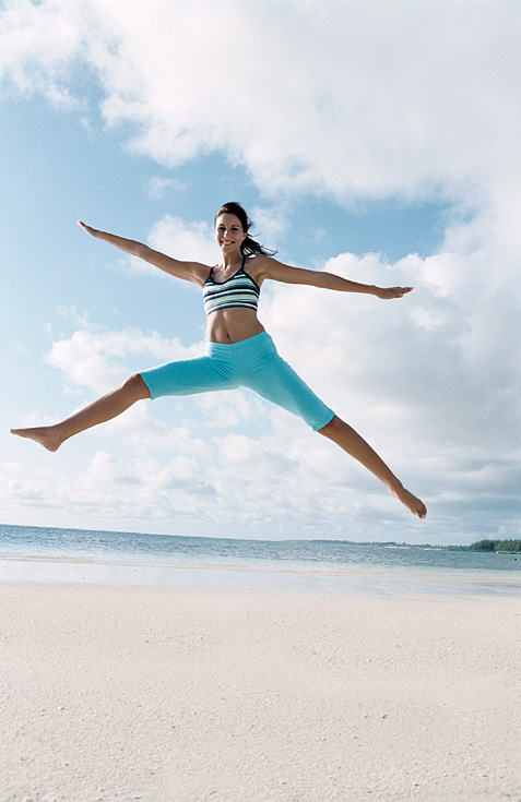 Image of woman jumping in the air at the beach.