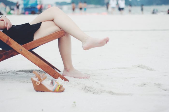 Image of woman sitting in a chair on the beach with her legs out.
